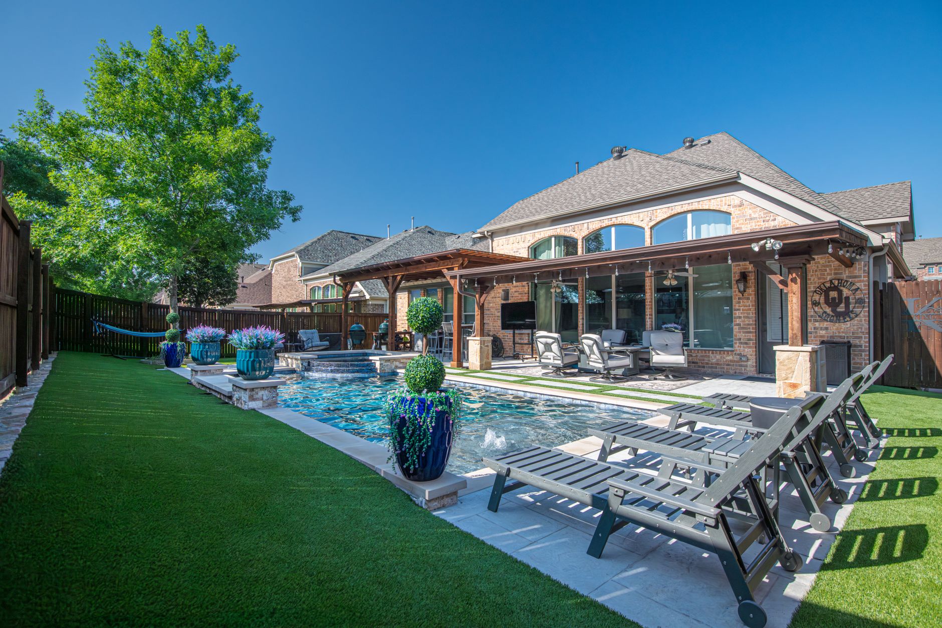 Elegant backyard in Roanoke, Texas with a modern swimming pool, deck chairs, and lush greenery.