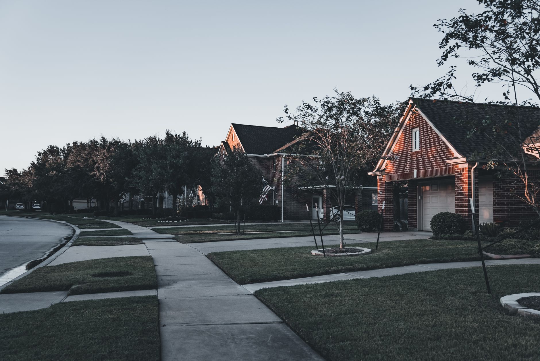 A serene suburban scene featuring brick houses and landscaped lawns at dusk.