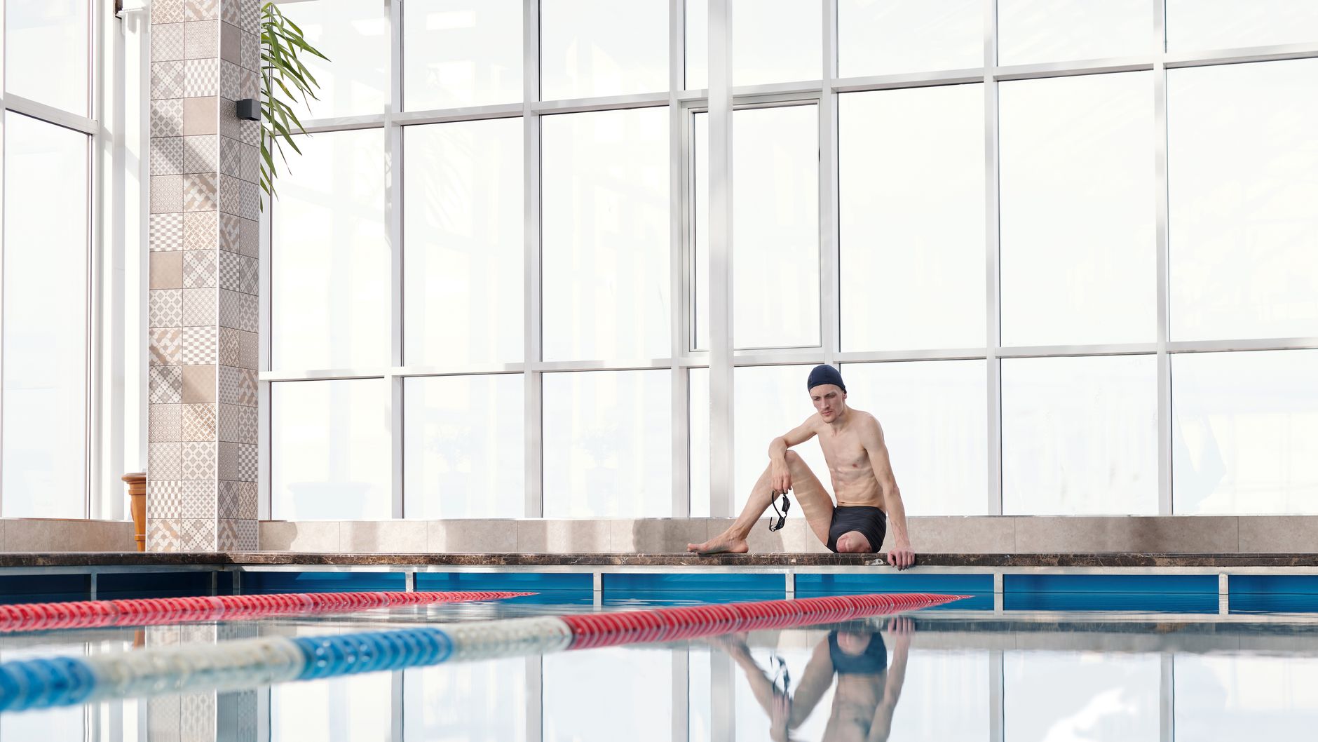 An adaptive athlete resting by an indoor pool, ready for a swimming workout.