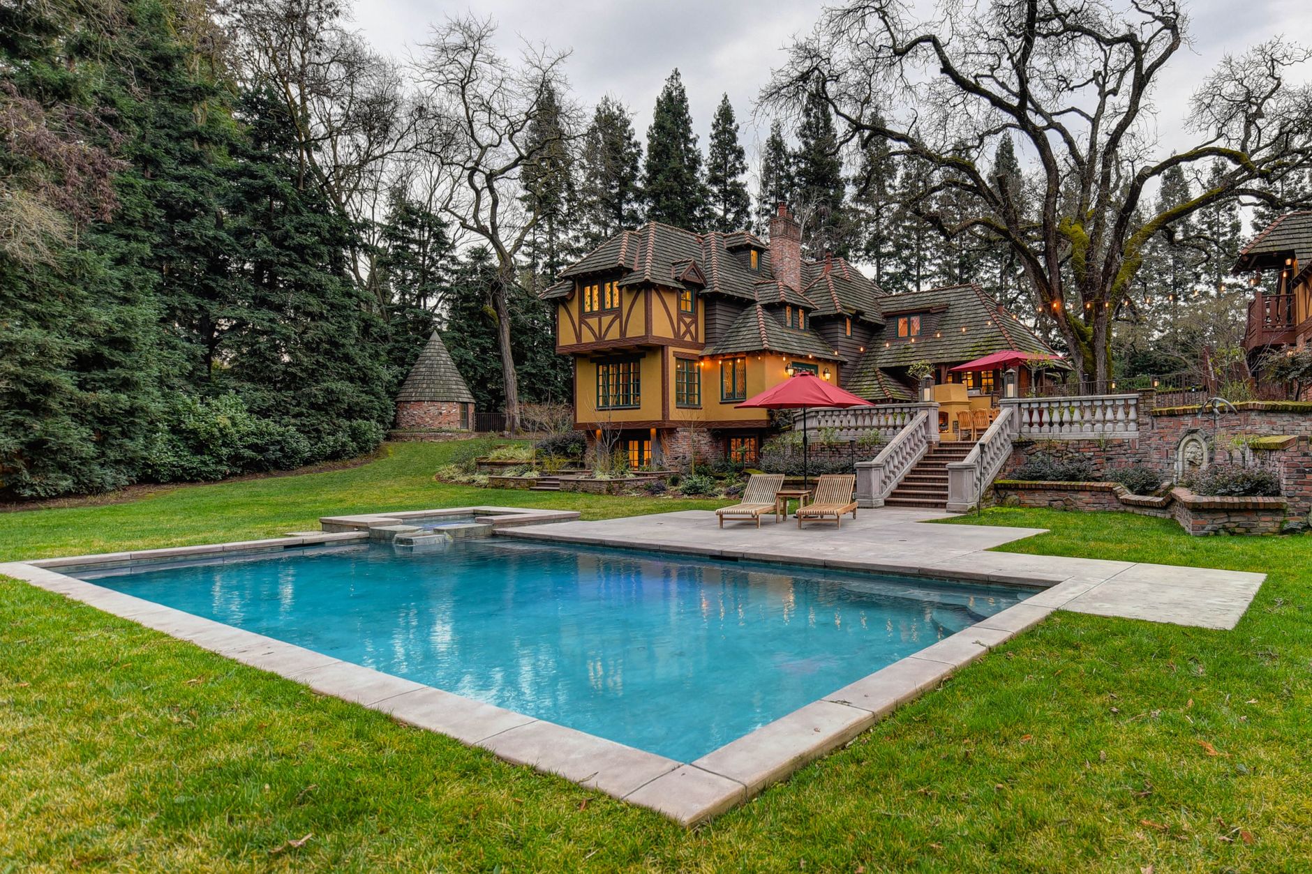 Stunning Tudor-style mansion with a pool, lush garden, and vibrant summer scenery.