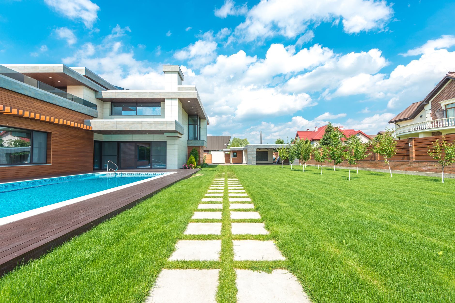 A stunning modern suburban home with a sleek swimming pool and lush green lawn under a blue sky.