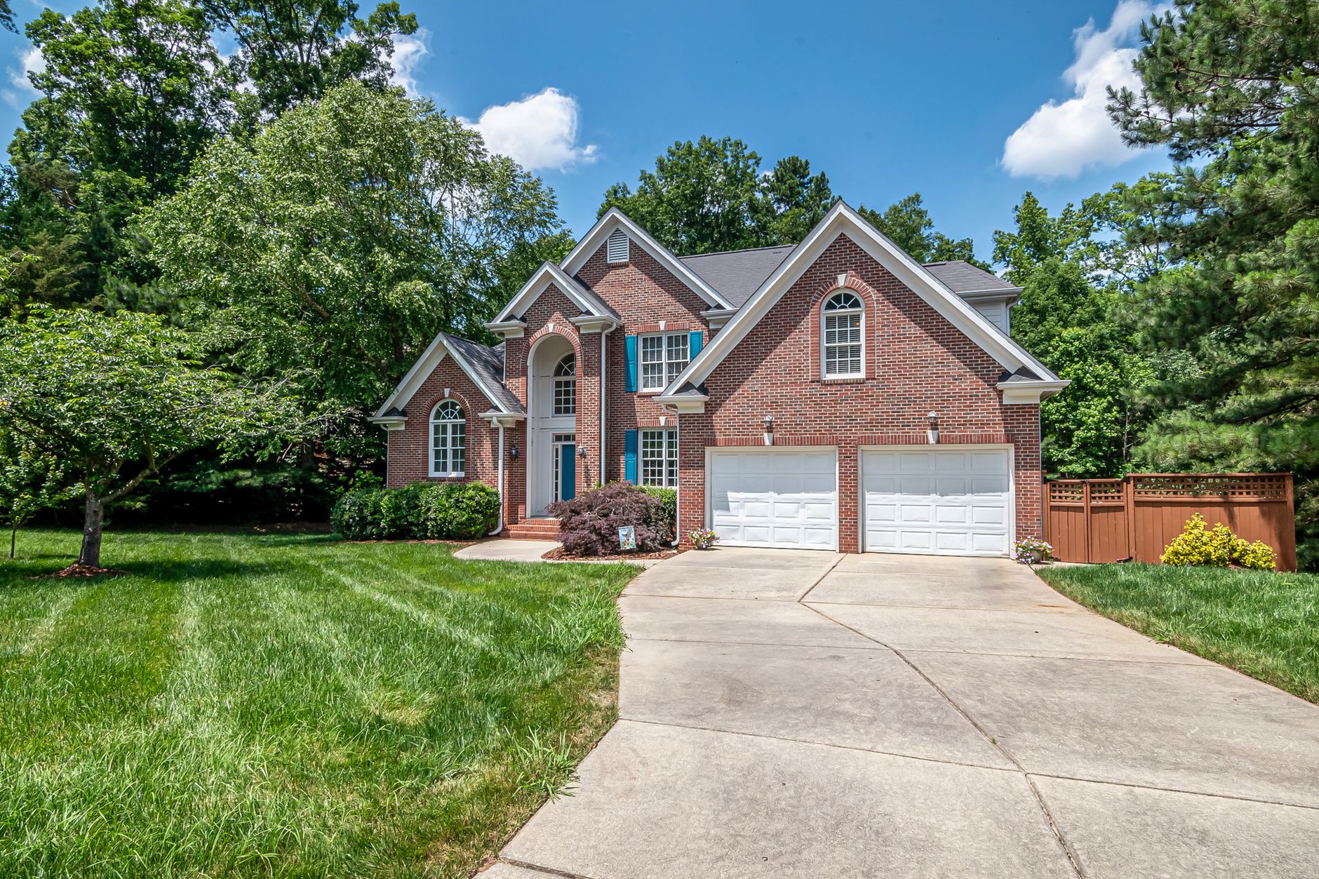 Beautiful brick house with double garage and lush green surroundings under a clear blue sky.